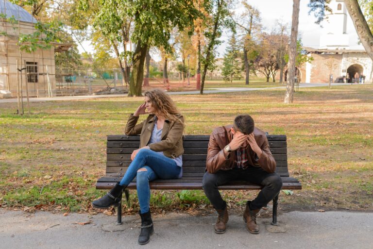 An upset couple seated on a park bench, expressing frustration during an autumn day.disputes de couple, thérapie de couple, communication dans le couple, conflit conjugal, psychologue en ligne, consultation en visio, relation de couple, psychologue clinicienne